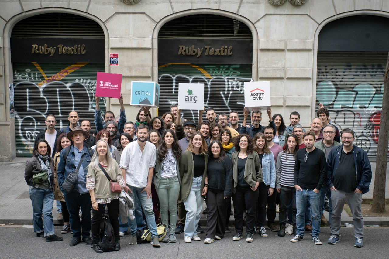 Una seixantena de persones posen al carrer davant d'un local tancat amb persianes grafitades sota tres arcs de pedra.